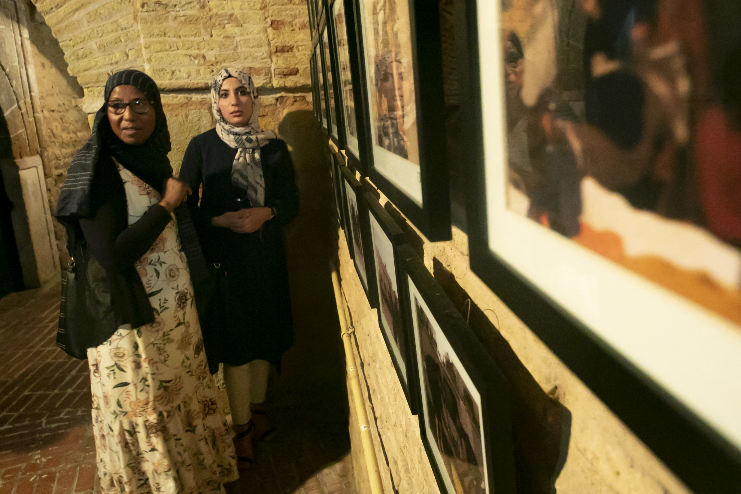 Two women in a room, standing to the left of artwork mounted on a stone wall. 