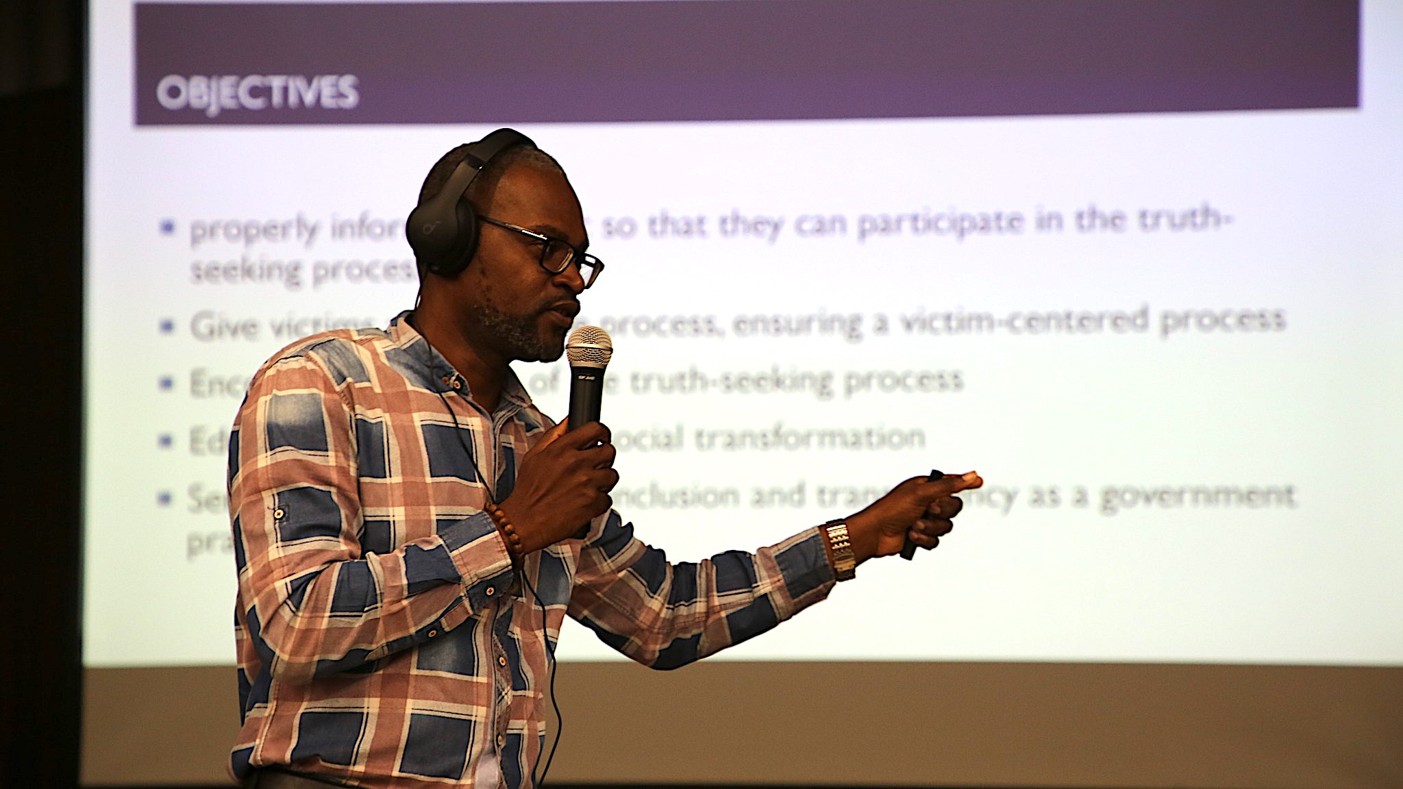 Un hombre se para frente a una pantalla con una presentación sosteniendo un micrófono.