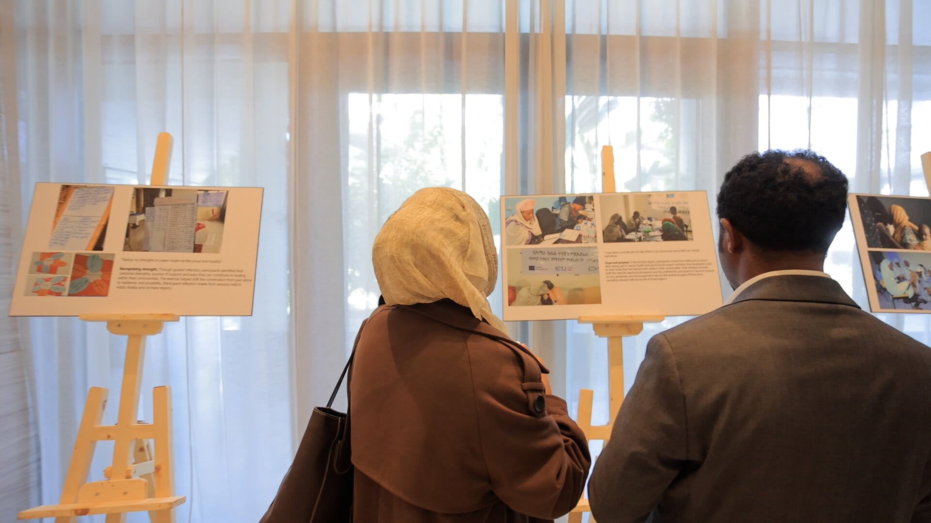 Two people stand, back toward camera, and look at poster on an easel.