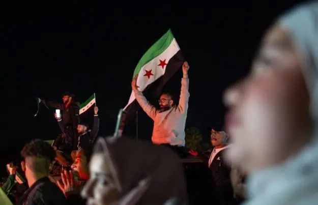 In a crowd of people, a man waves the Syrian flag