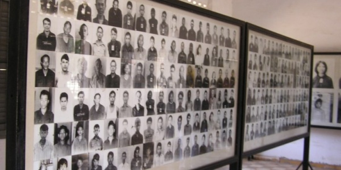 A grid of photos displayed on a board of people killed by the Khmer Rouge in a room.