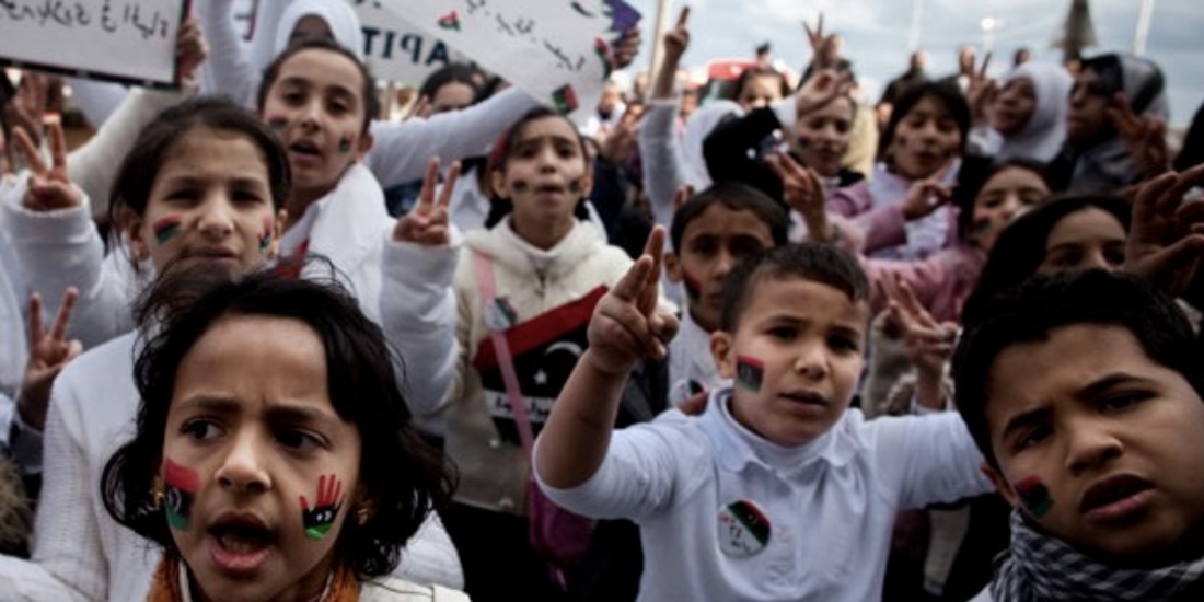 Children at a rally holding up posters and peace signs, with their faces painted in red, black, and green. 