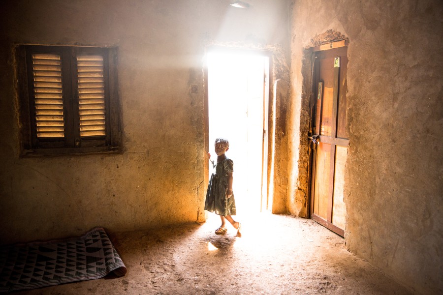 A young girl stands in the doorway to her house