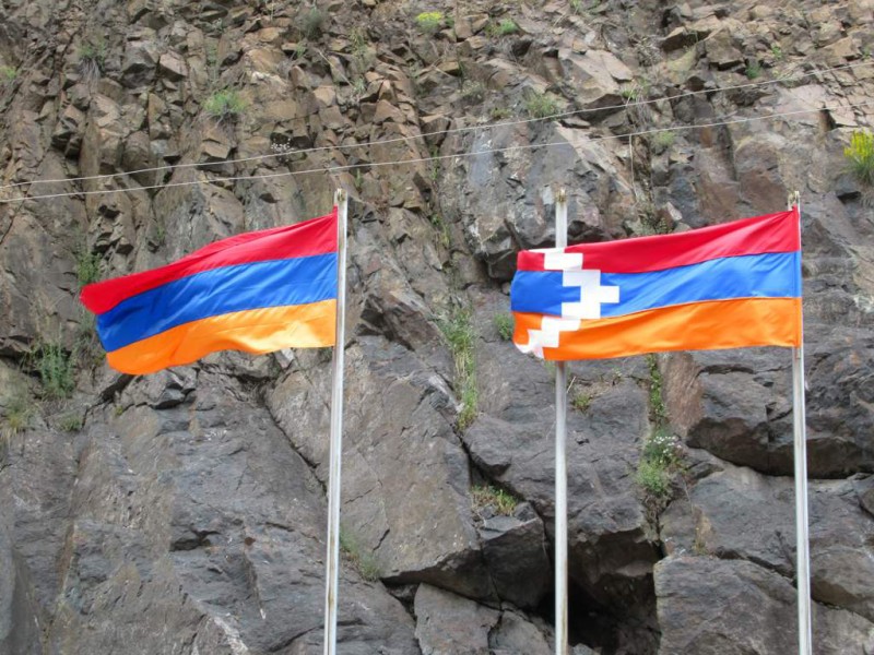 Two flags stand against a rocky mountainside.