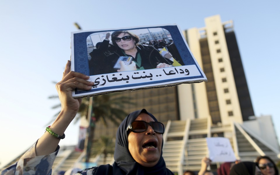 A woman in a headscarf and sunglasses holds up a placard with a photograph of women and writing in Arabic.