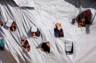 Image of Children looking through holes in a tent at al-Hol displacement camp in Hasaka governorate, Syria, on April 2, 2019.