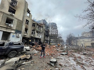 A man stands on a street in Kharkiv, Ukraine, surrounded by destroyed buildings and rubble.