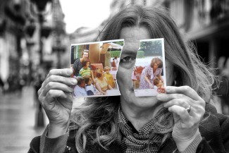 A woman holds up two halves of a ripped photograph and looks out from between them.