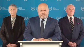 ICC Prosecutor Karim Khan stares front and center at the camera, flanked by one official on each side. 