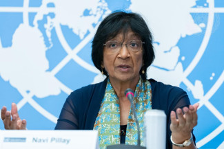 Navi Pillay looks at the camera while speaking. A large UN emblem is in the background.