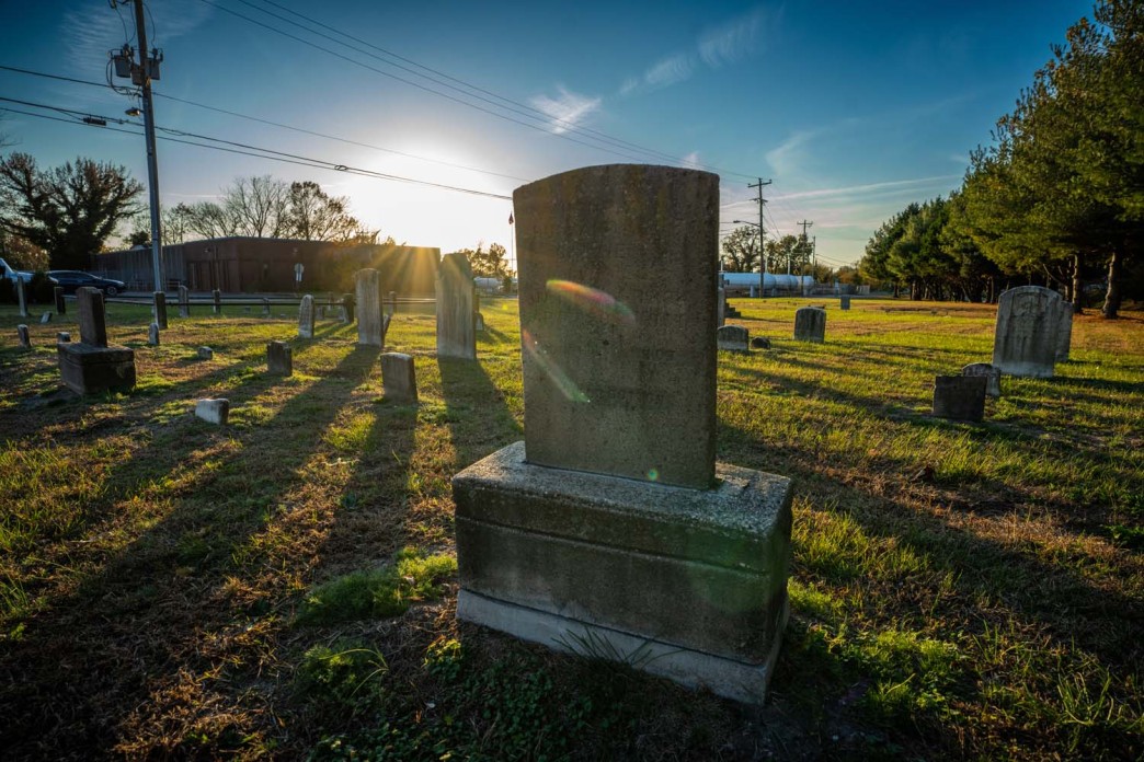 A gravestone stands in graveyard as the sun sets.