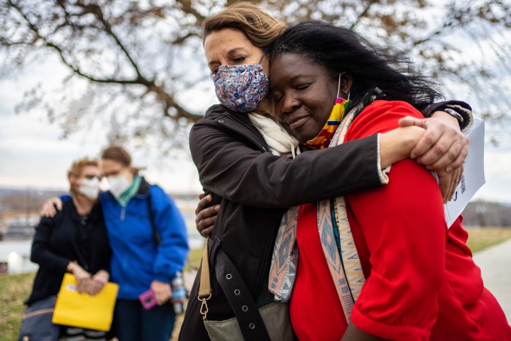 Two women embrace near a tree outside.