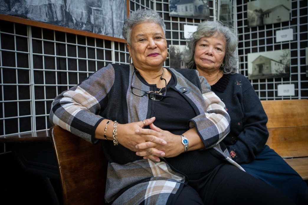 Two women sit side by side on a bench facing the camera.