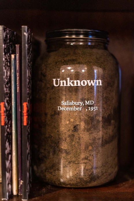 A clear jar filled with dirt and with the word "Unknown" written in white sits on a shelf.