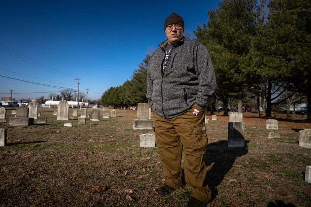 A man stands in a graveyard looking directly at the camera.