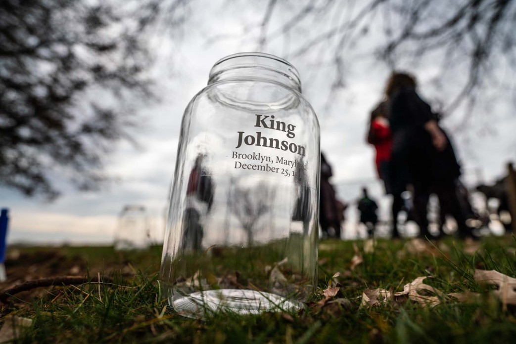 A clear empty jar with "King Johnson" written on it in black ink sits in the grass outside.
