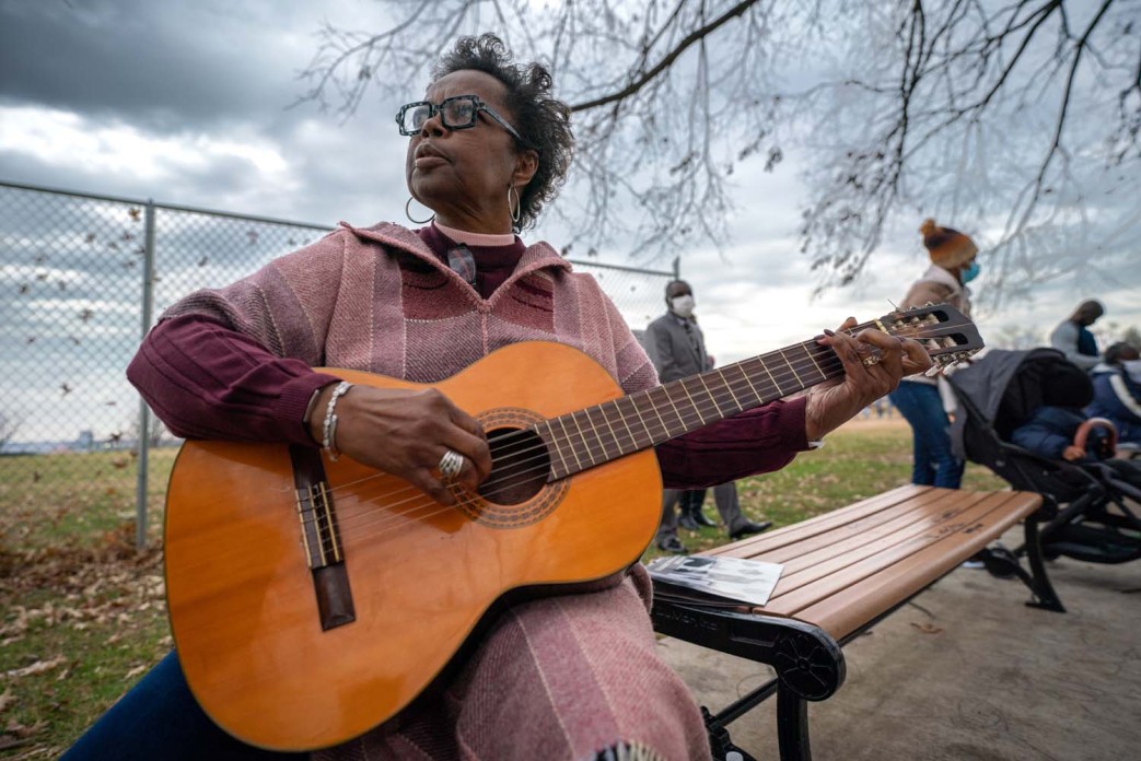 A woman in a pink dress sits on bench holding a guitar and playing it.
