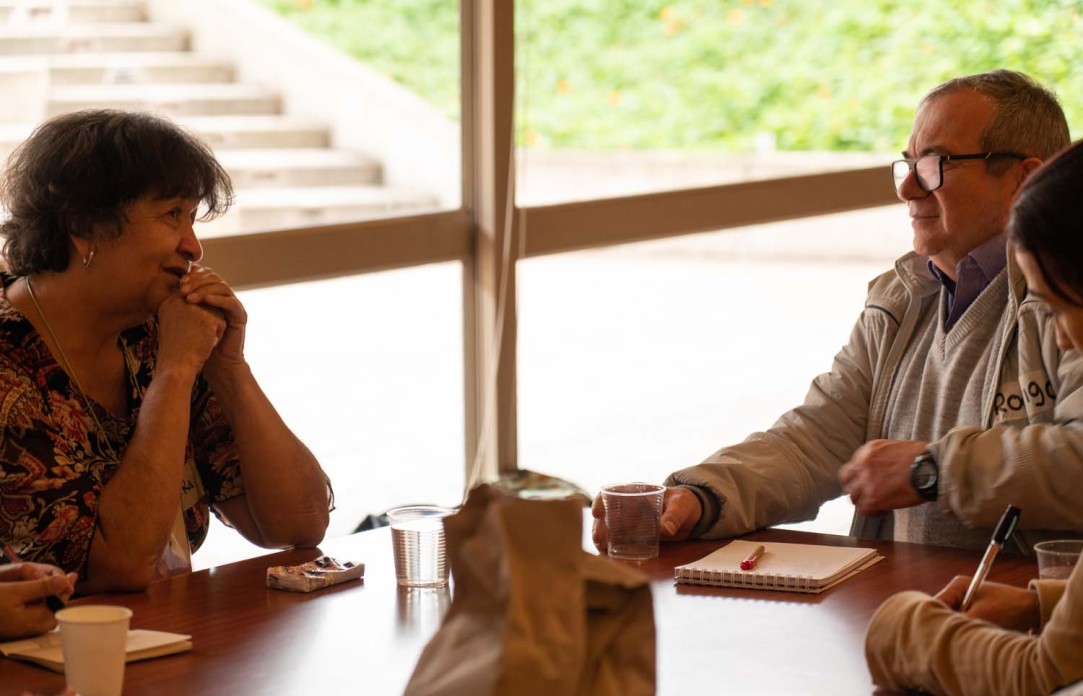 A woman on the left faces a man on the right across a table as they talk.