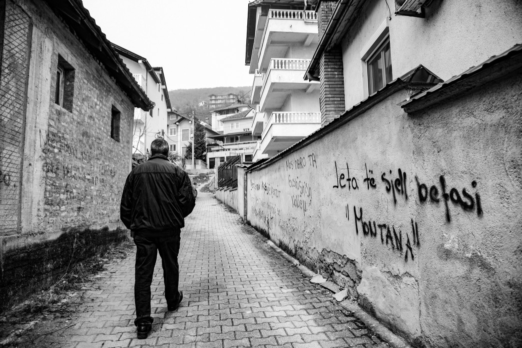 Black and white photo of a man walking down a narrow street.