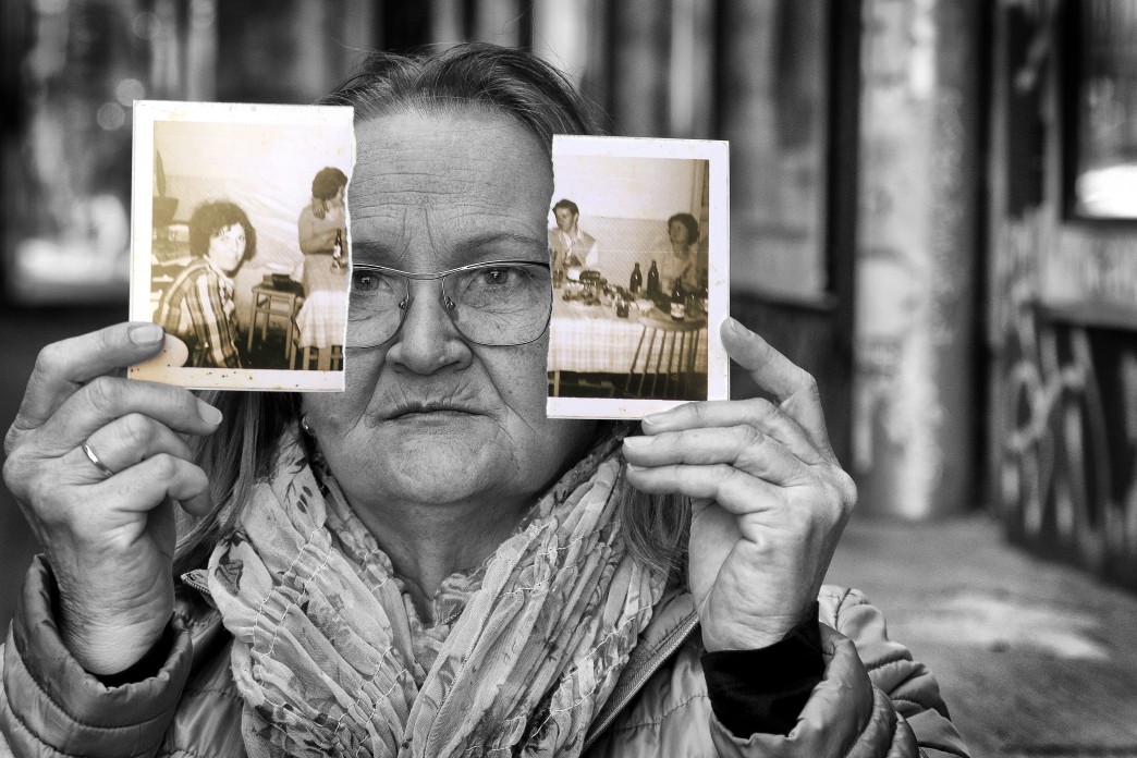 An older woman holds up a photograph of a family that has been torn in half.