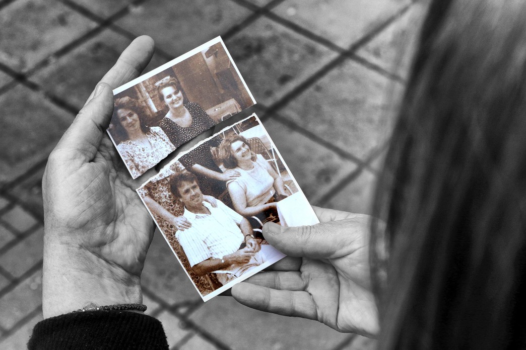 A woman holds two halves of a ripped photograph together.