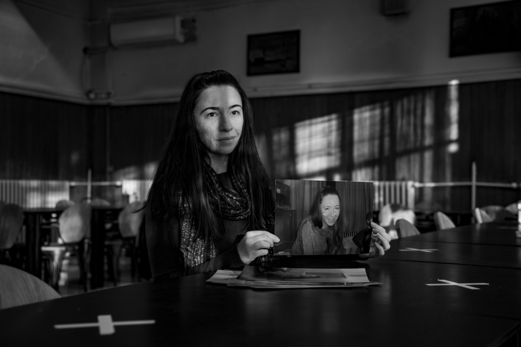 A woman sitting at a table holds up an 8x10 photograph of a woman that looks like her.