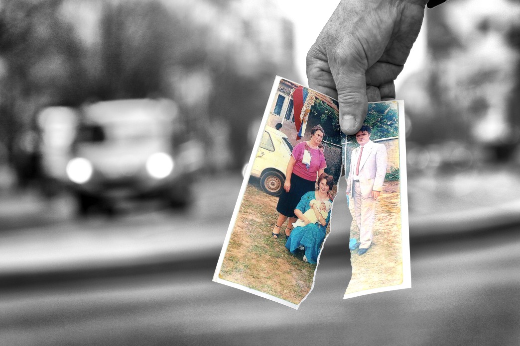 A single hand holds two ripped halves of a photograph together.