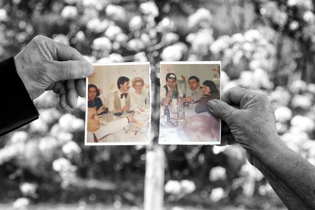A hand on the left holds the left half of a ripped photograph, with a different hand on the right holding up the right half of the photograph.