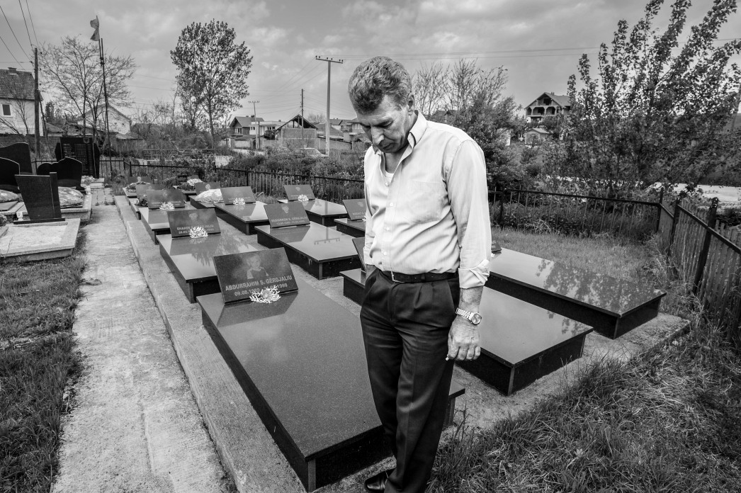 A man stands with his head bowed in the middle of a cemetery.
