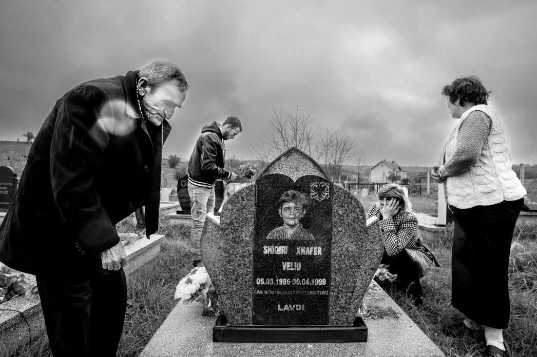 A family visits the gravestone of a child, crying and laying flowers.