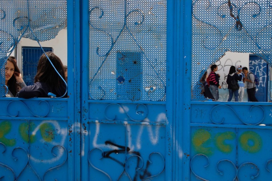 Youth are visible through openings in a bright blue metal gate.