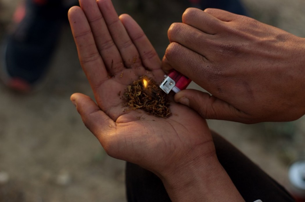 A close up of two hands, one hand holds a lit lighter to a palmful of hashish.