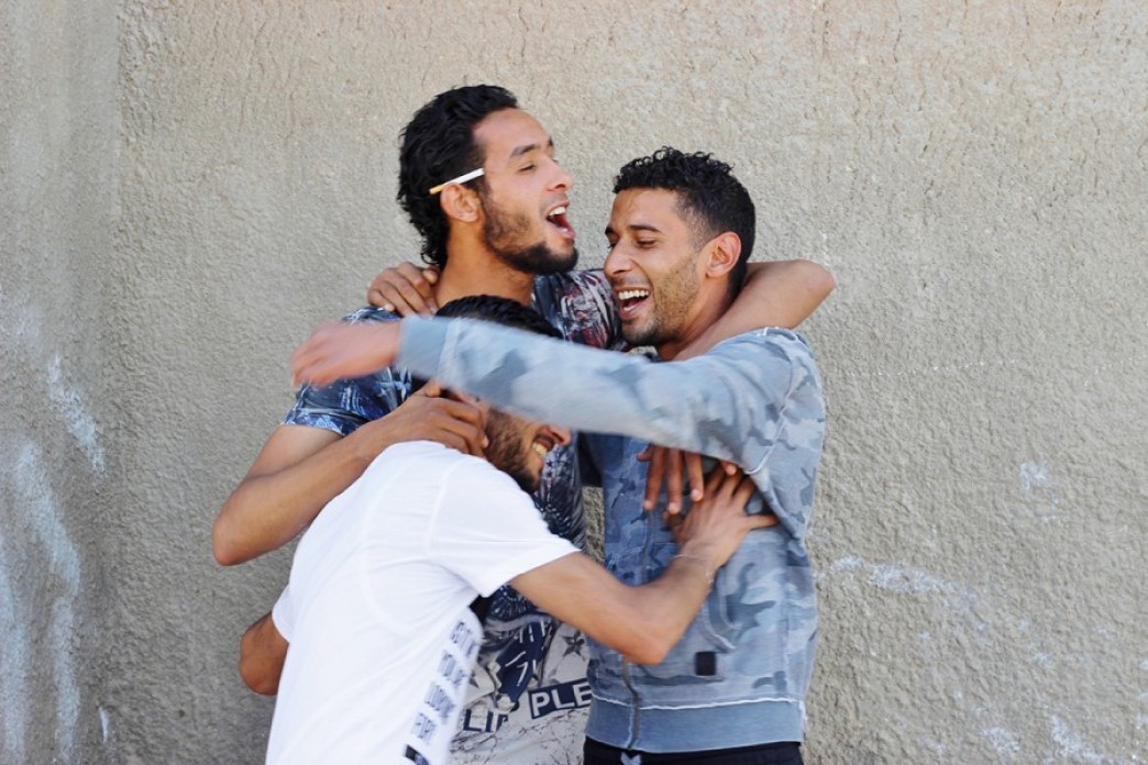 Three young men embrace, laughing.