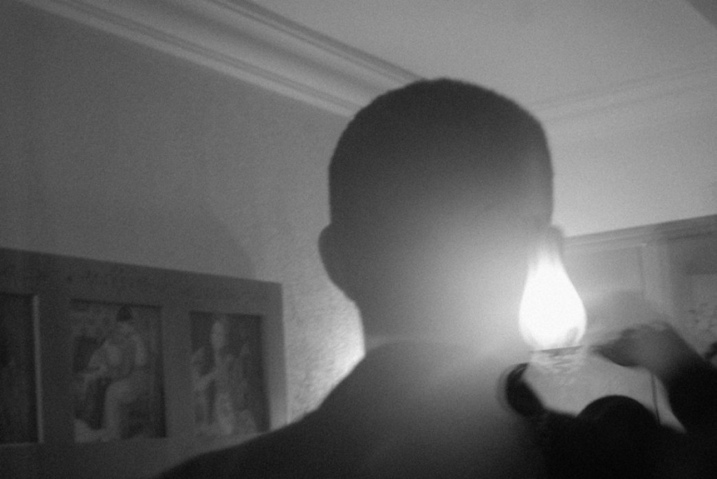 A layered image with the silhouette of a person in a room with a naked light bulb in black and white.