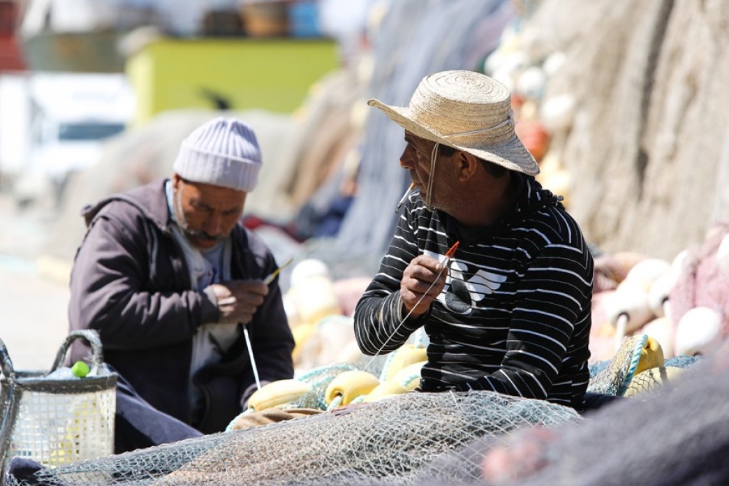 Two fishermen sew a net with the hope that something will change.